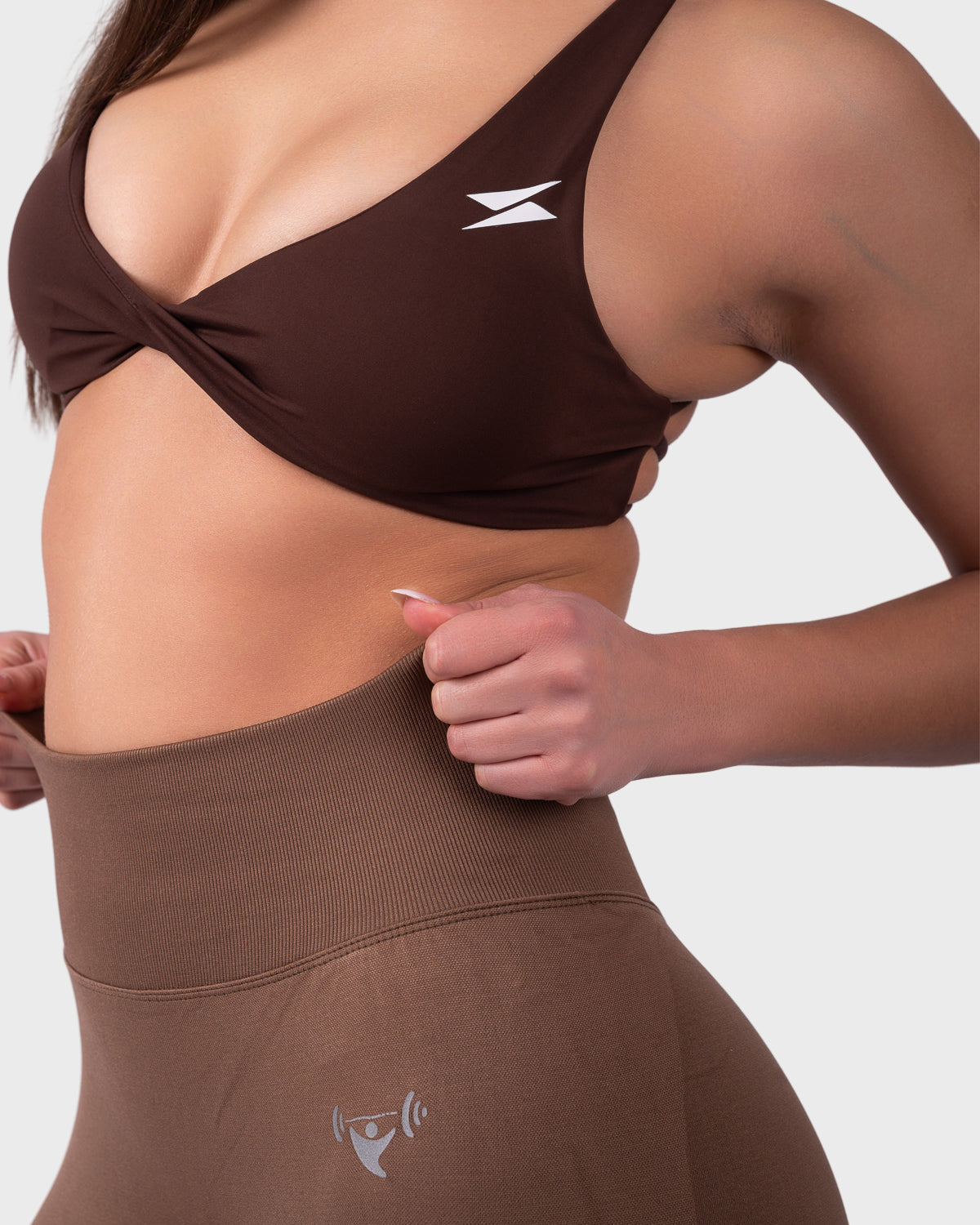 Close-up side view of brown bra and leggings, showcasing texture and logo detail.