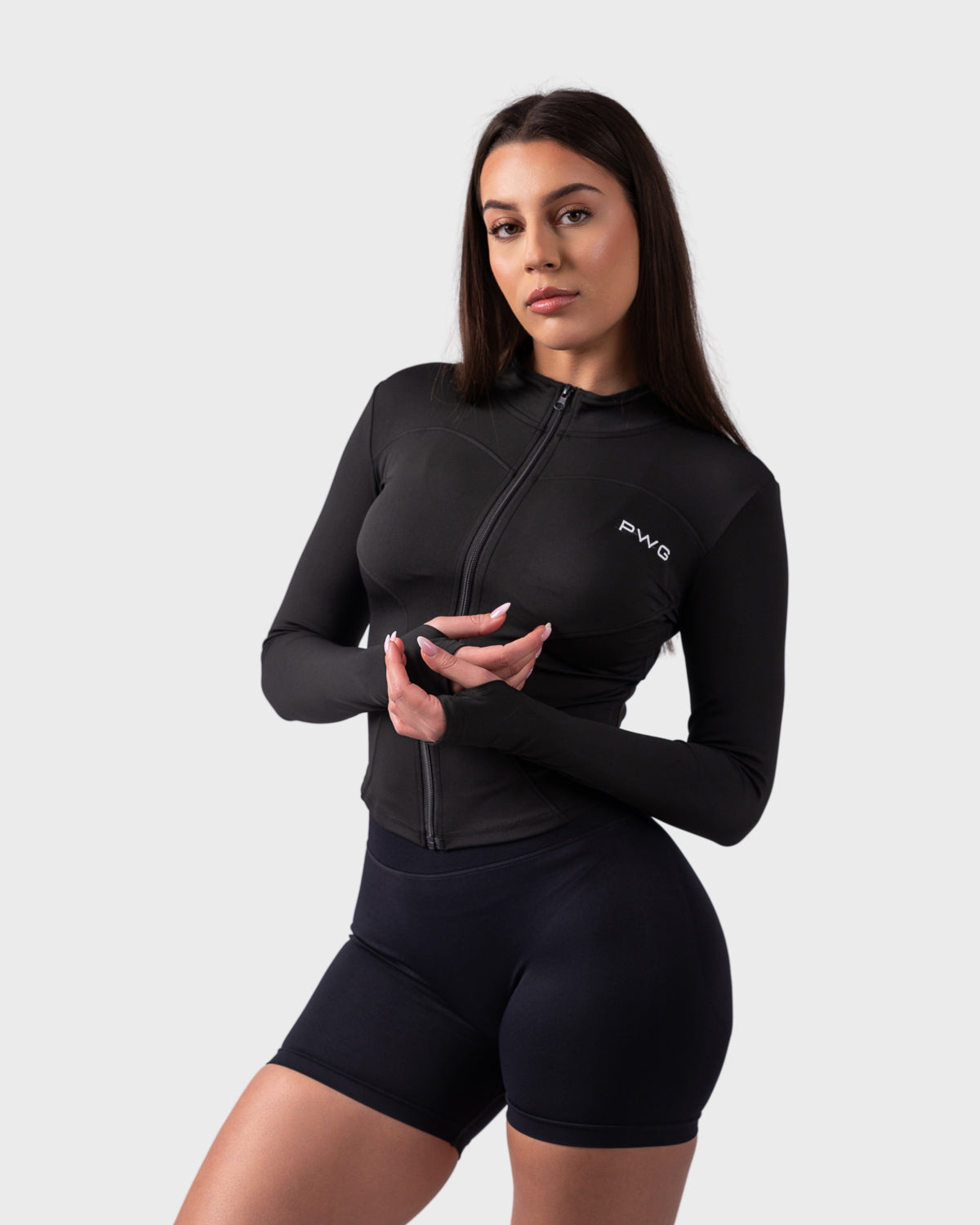 Side pose in black sculpt jacket, hands clasped, styled with high-rise shorts.