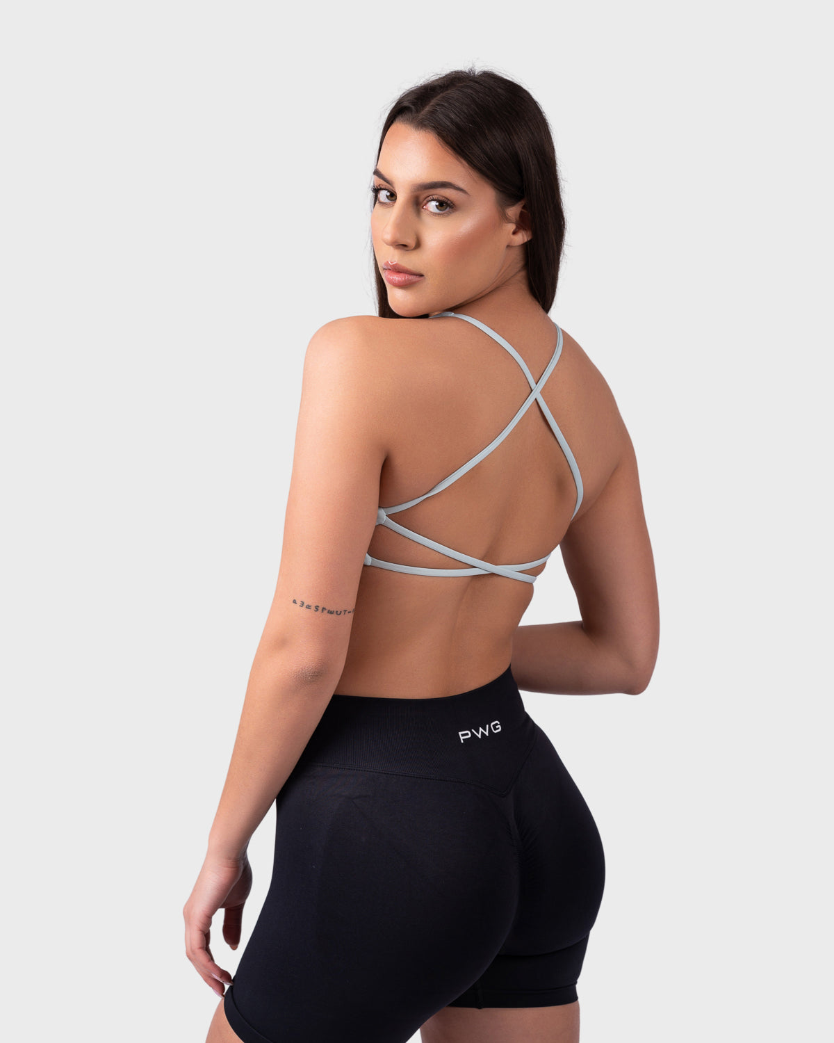 Back-side profile of model wearing celeste bra with black shorts, relaxed stance.