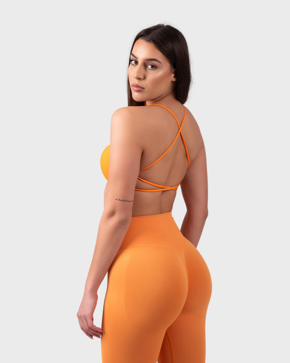 Rear view of neon orange backless sports bra, open back with cross straps.