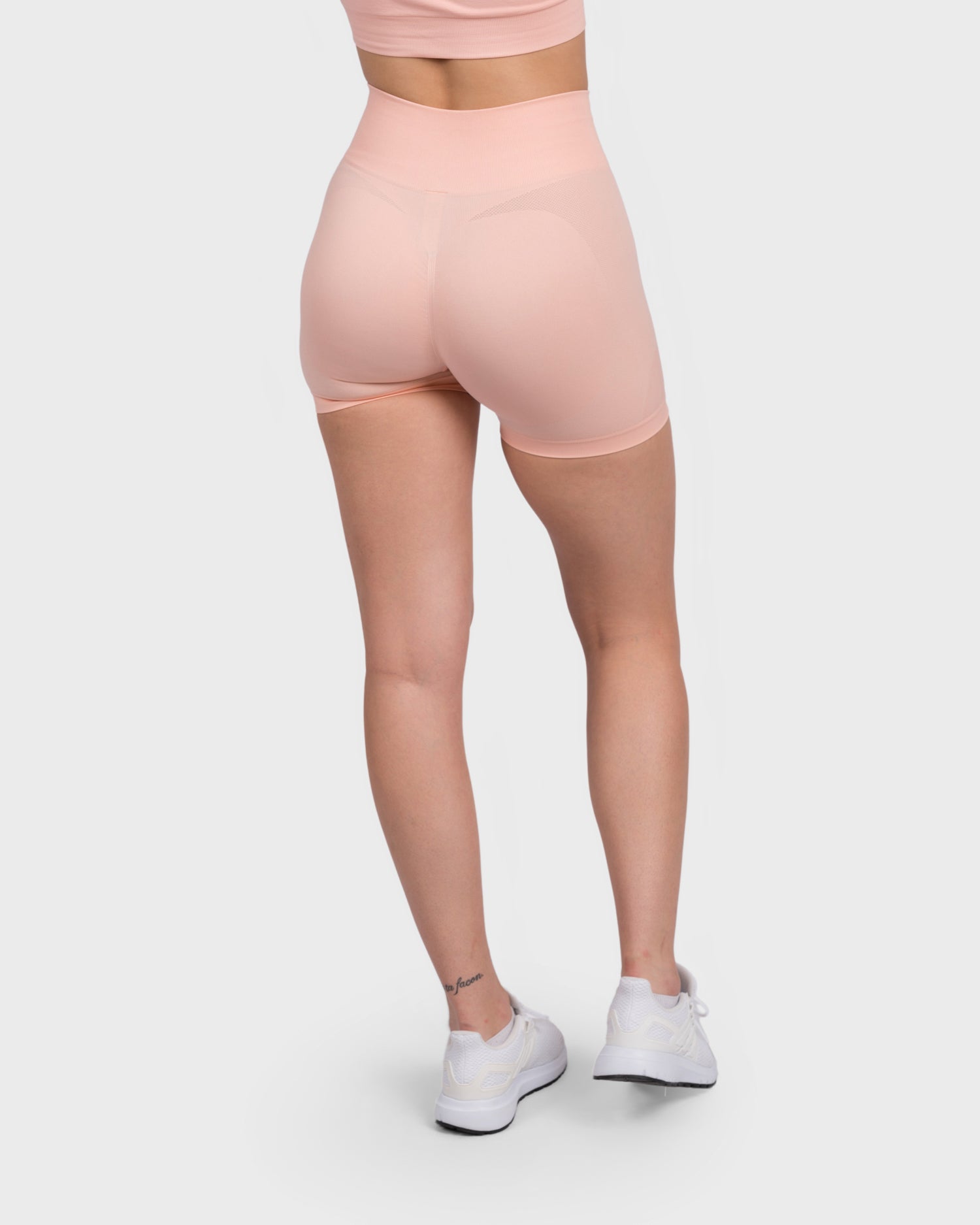 Back view of FlexActive High Waist Shorts in light peach, styled with white sneakers.