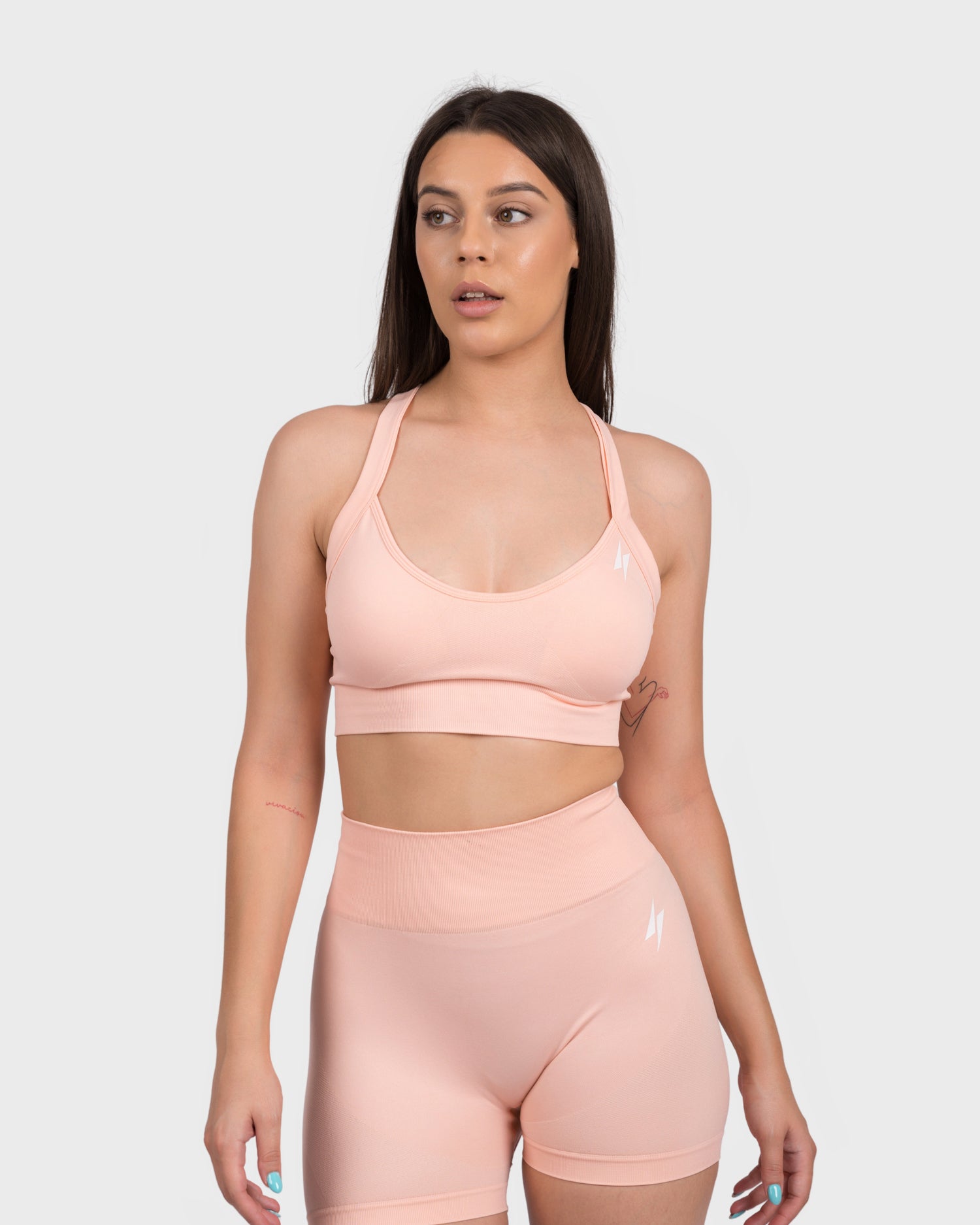 Model wearing the FlexActive Sports Bra - Light Peach and matching high-waisted biker shorts, posing front-facing to highlight the seamless, supportive fit. This stylish activewear set features a sleek logo detail and is designed for comfort, performance, and gym workouts.
