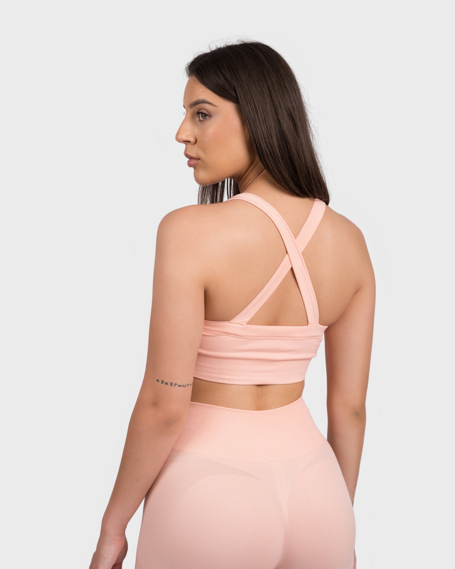 Model showcasing the back design of the FlexActive Sports Bra - Light Peach, featuring stylish crisscross straps for added support and a flattering fit. Paired with matching high-waisted biker shorts, this seamless activewear set is designed for comfort and performance in gym workouts and everyday wear.