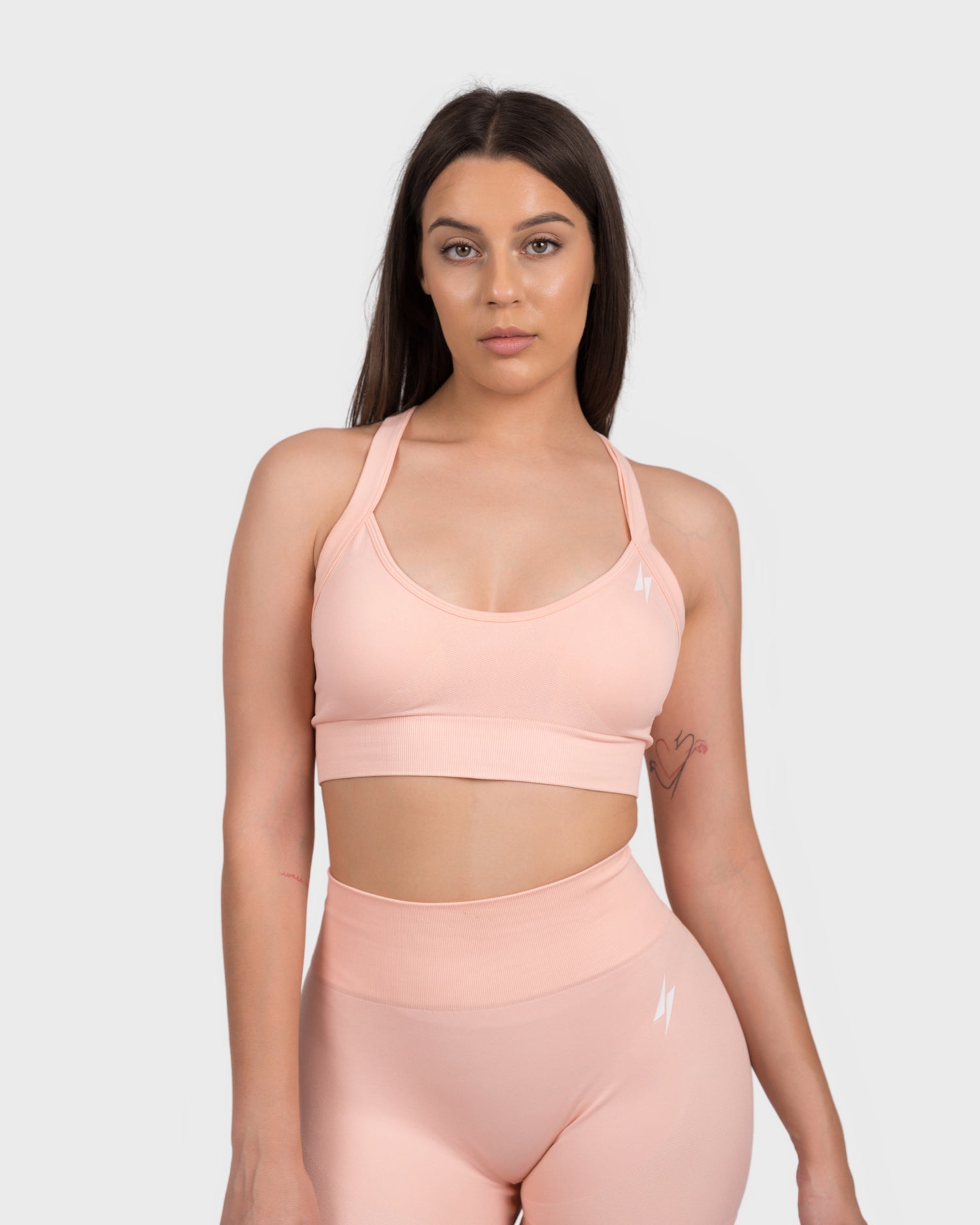 Model wearing the FlexActive Sports Bra - Light Peach and matching high-waisted biker shorts, posing front-facing to highlight the seamless, supportive fit. This stylish activewear set features a sleek logo detail and is designed for comfort, performance, and gym workouts.