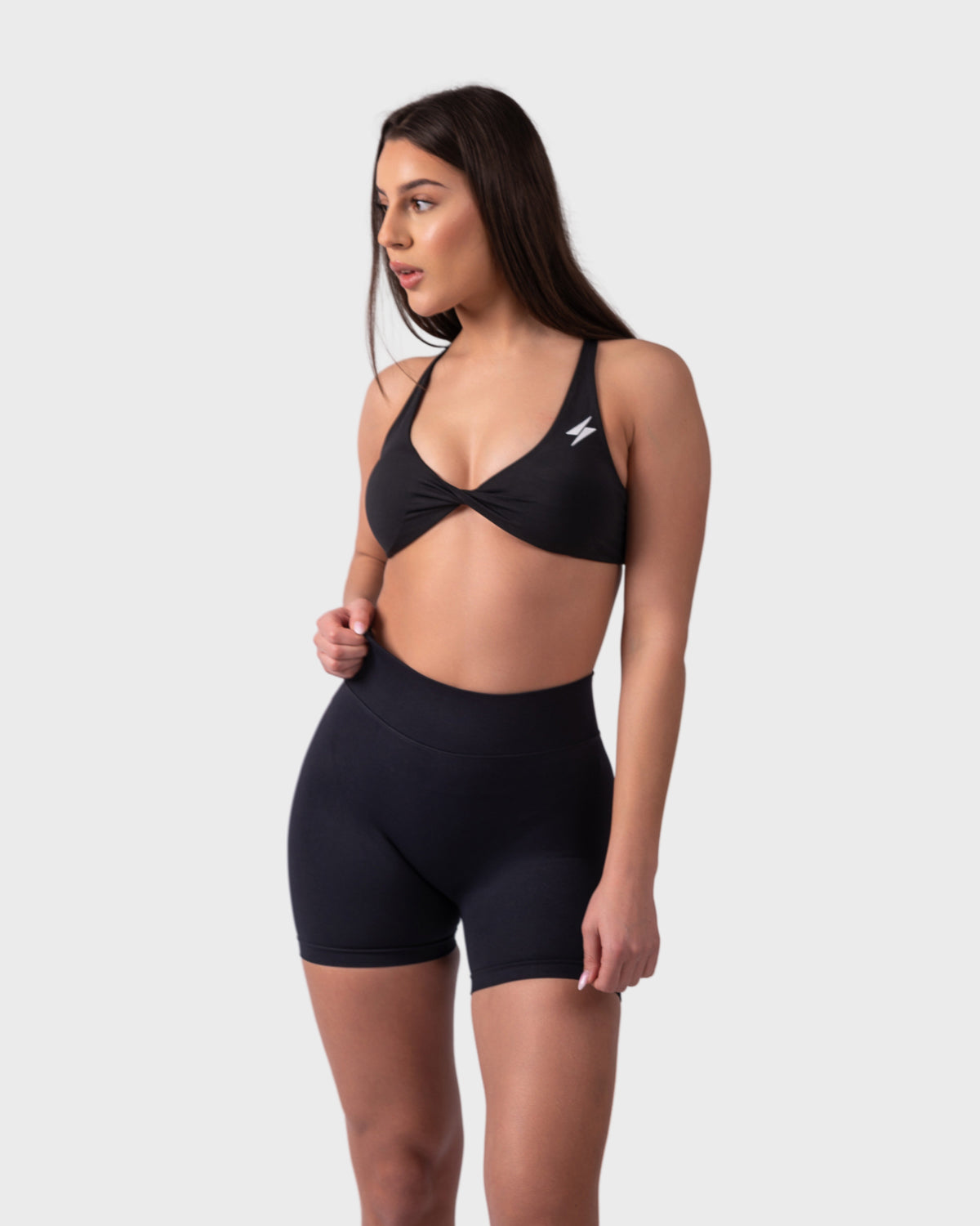 Full-body front pose in black sports bra and matching shorts, relaxed stance.