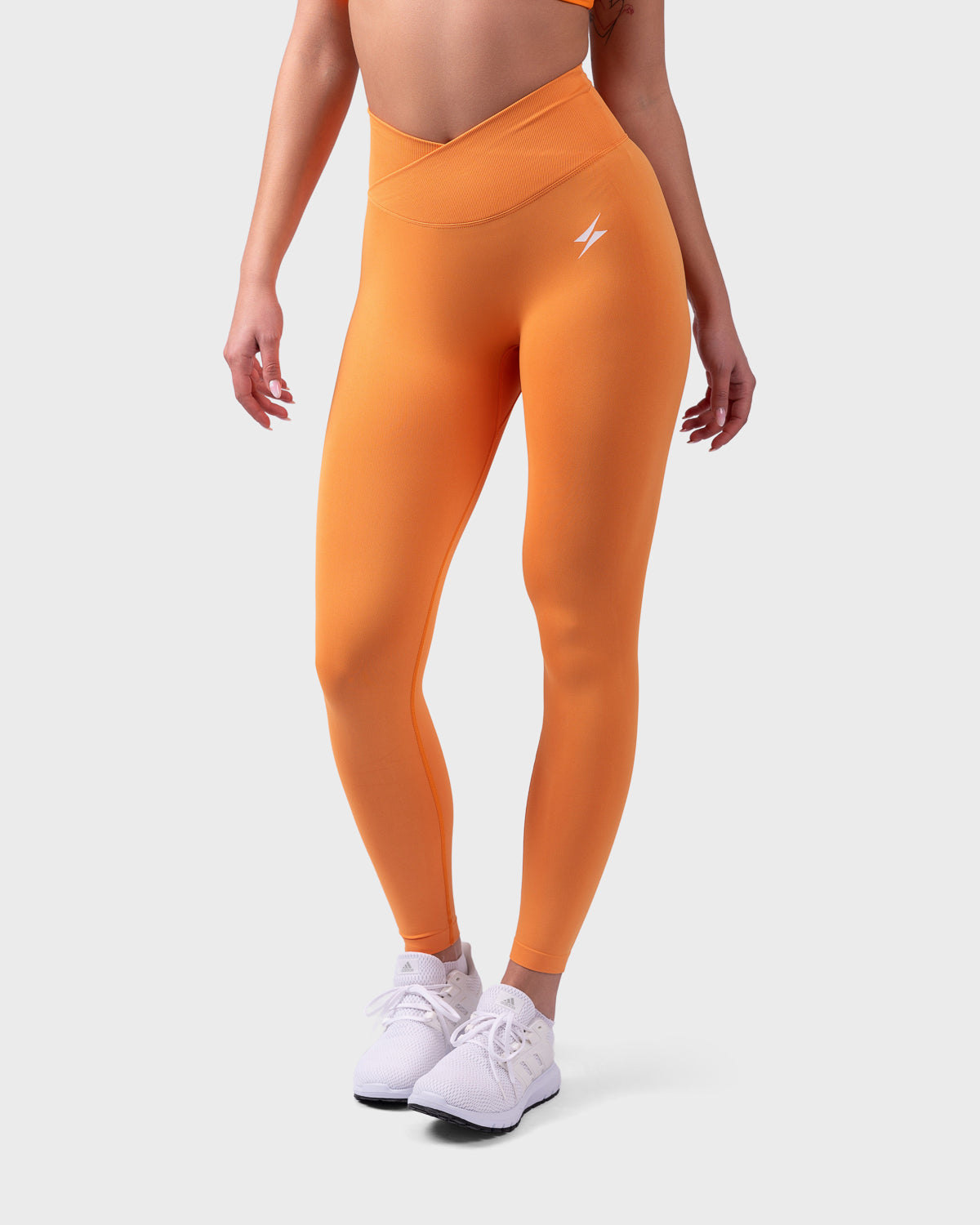 Evolve V-Sculpt Leggings from PWG Active in bright orange, front view with V-waistband and logo.