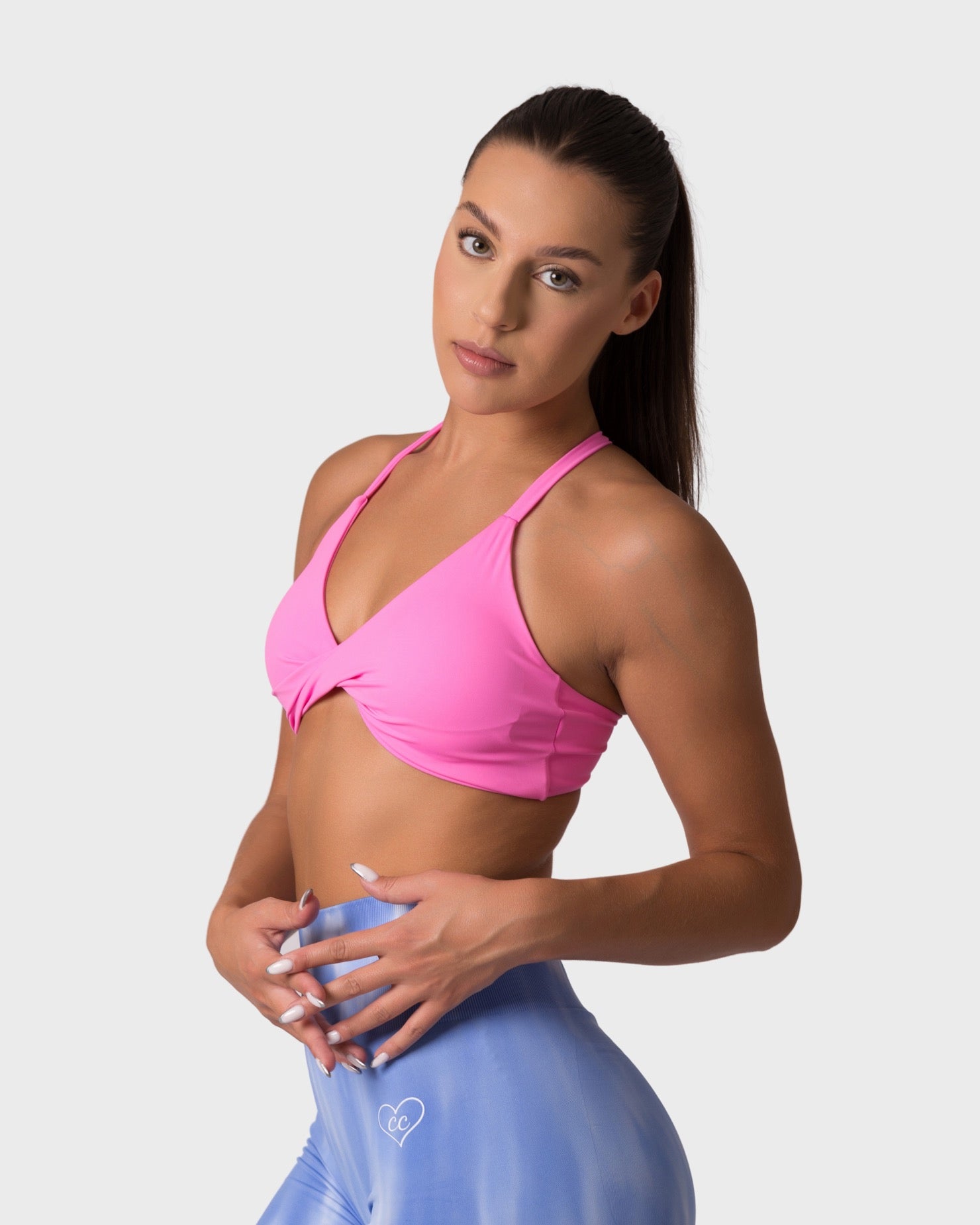 Front view of rose pink knitted sports bra with twist-front, paired with blue shorts.